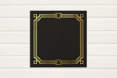 Gold art deco inspired square border design on a black square piece of paper. The paper sits on a white painted wood background.