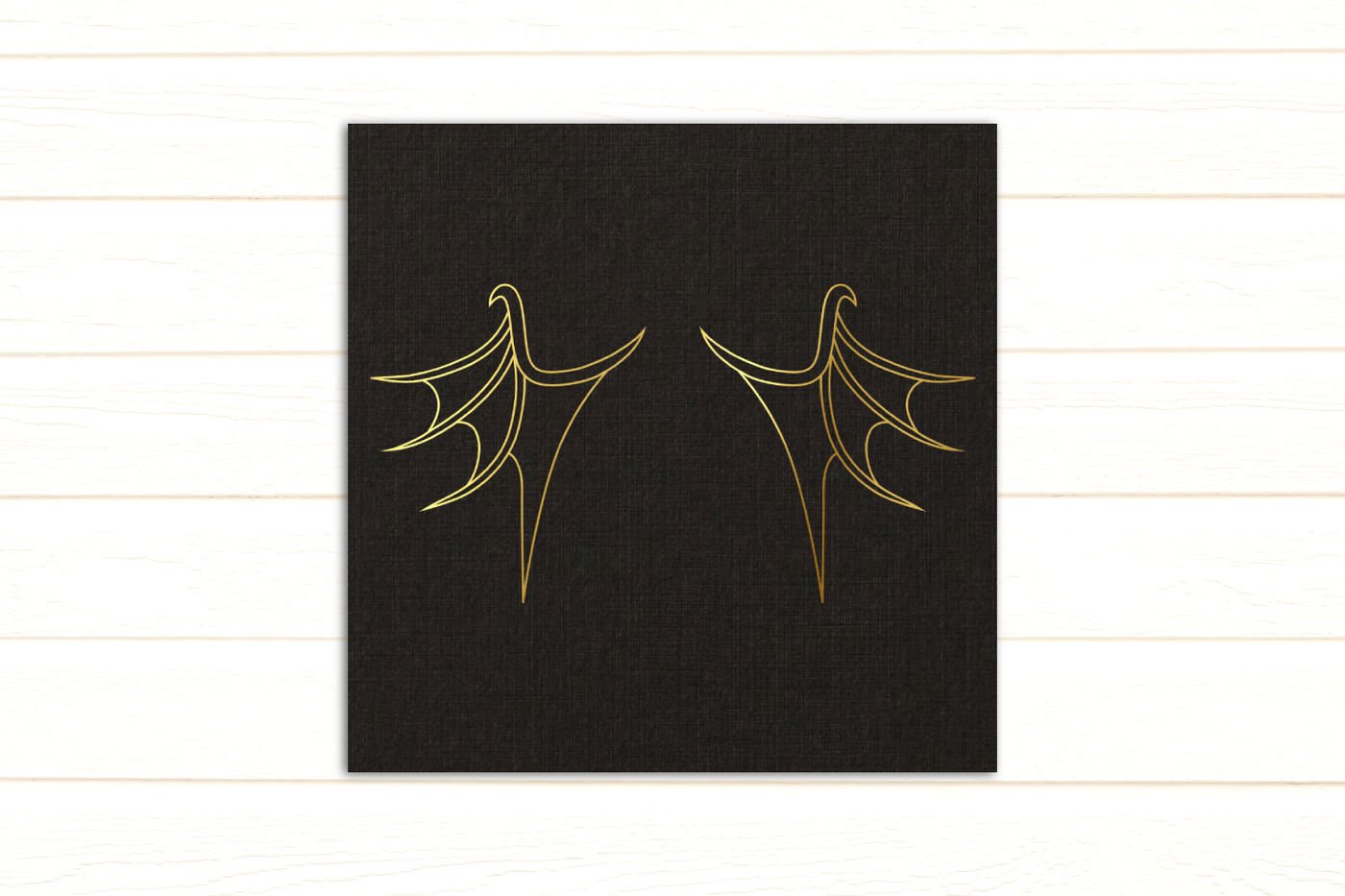 Line drawing of dragon wings on gold foil on black paper.