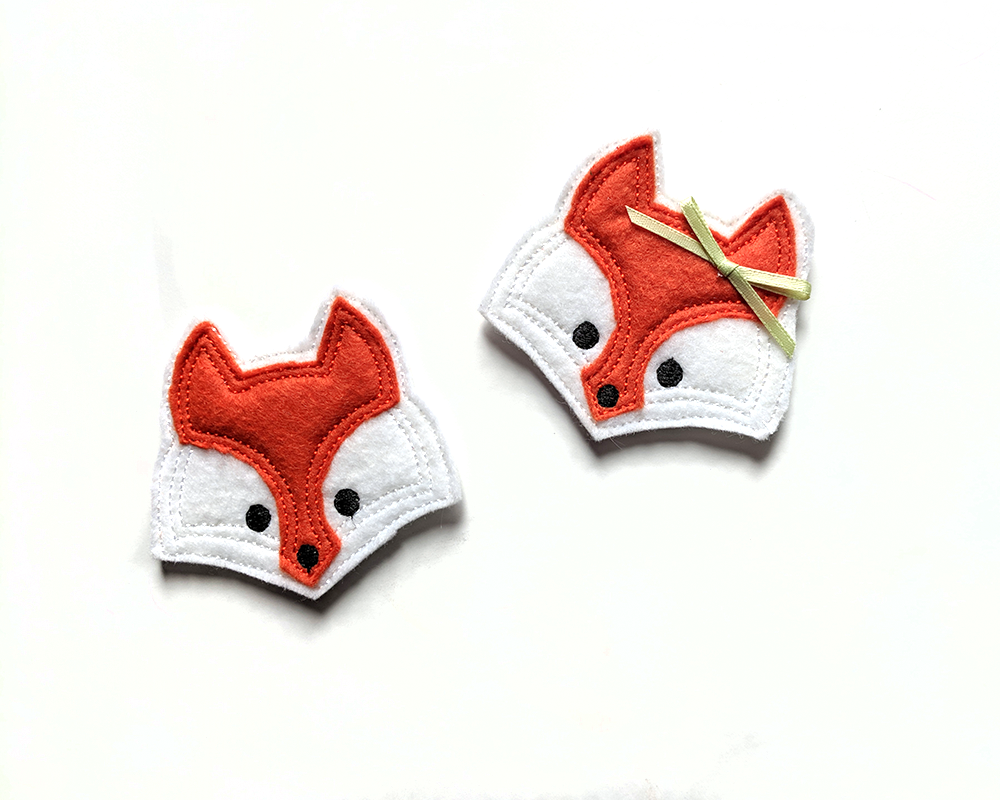 Fox face felties on a white background. One has a real green bow added.