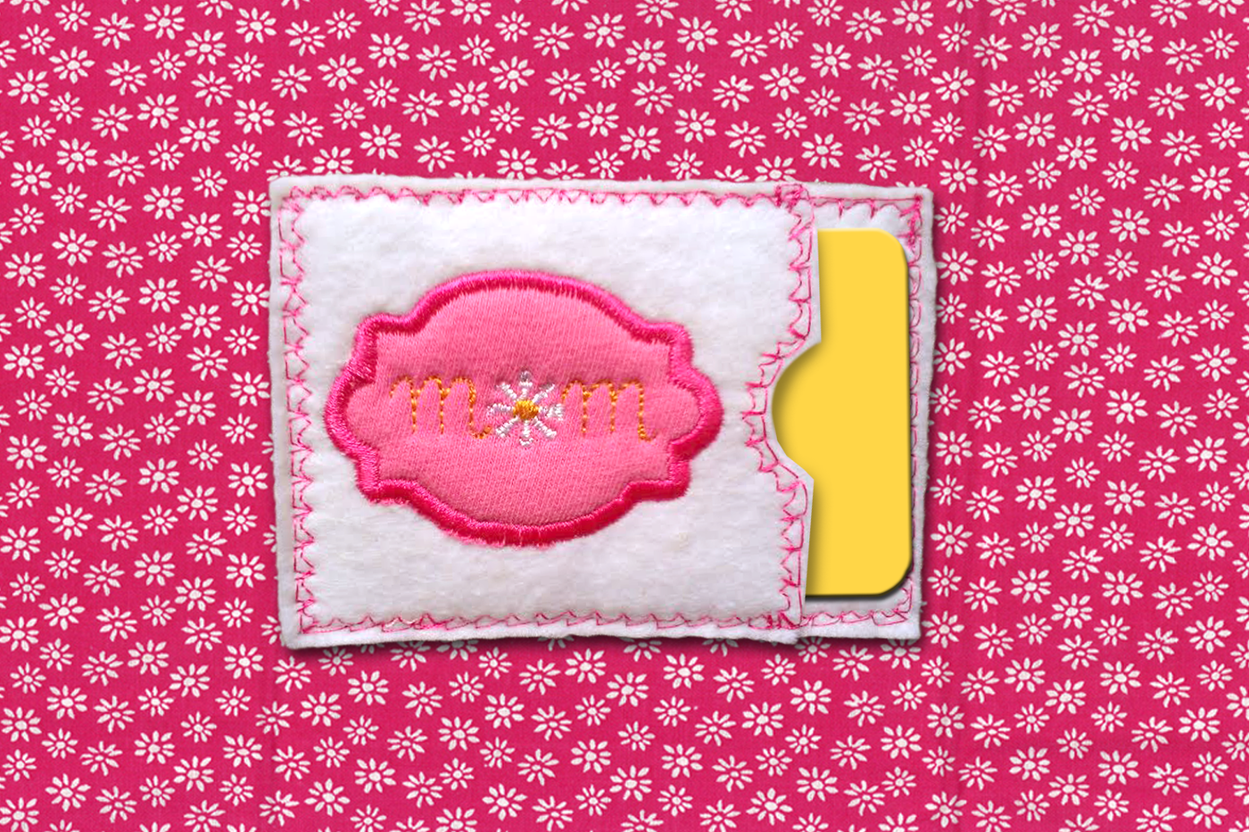 Felt gift card holder. It says "MOM" with a flower for the O and a decorative applique frame around the word.