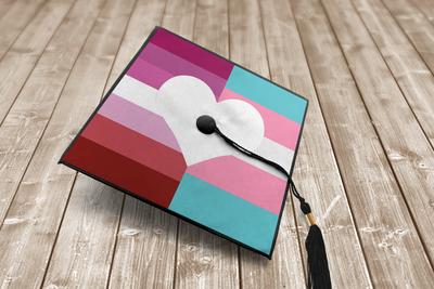 Grad cap with a large heart in the middle. Behind the heart on the left half are stripes in the color of the lesbian flag, and on the right stripes in the color of the trans flag.