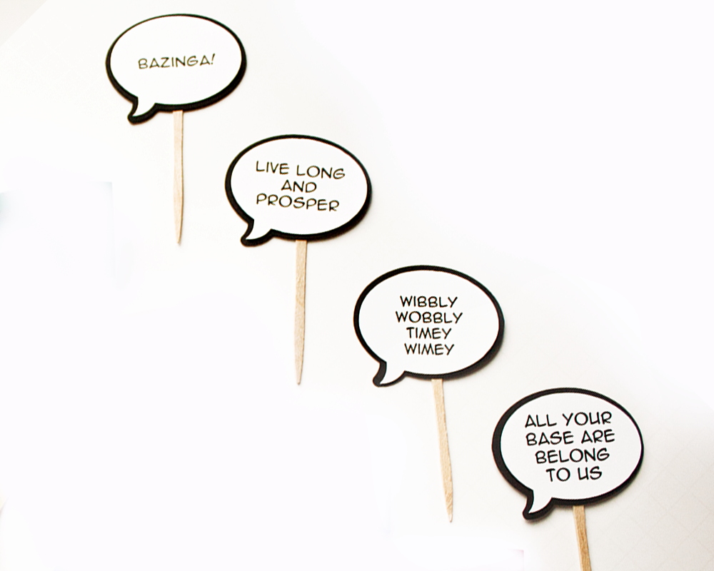Four cupcake toppers that look like comic book speech bubbles. Each has a different geeky phrase.
