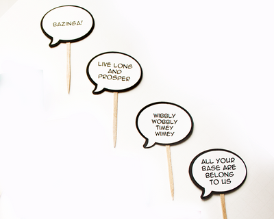 Four cupcake toppers that look like comic book speech bubbles. Each has a different geeky phrase.