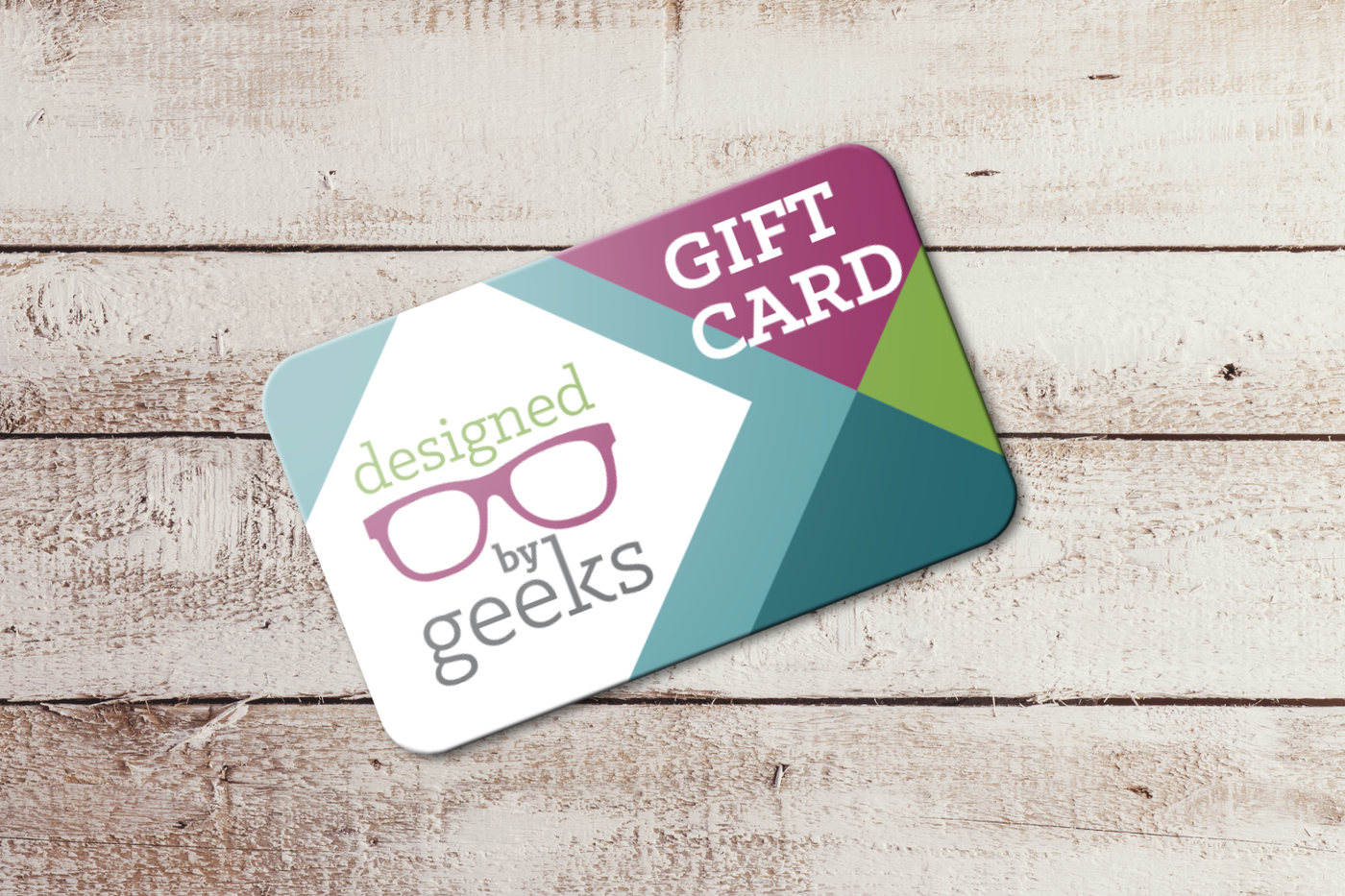 Gift card laying on a wood surface. It has the Designed by Geeks logo and geometric graphics in the brand colors.
