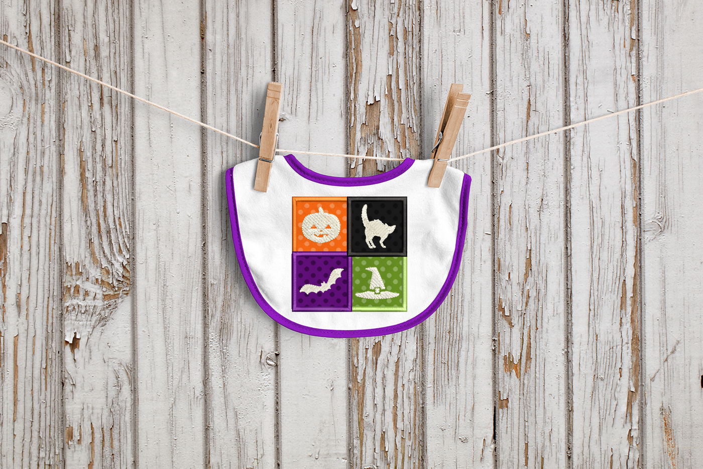 Bib with 4 applique squares in different Halloween colors. In the middle of each square is a white embroidered design: a carved pumpkin, scared cat, flying bat, and witch hat.