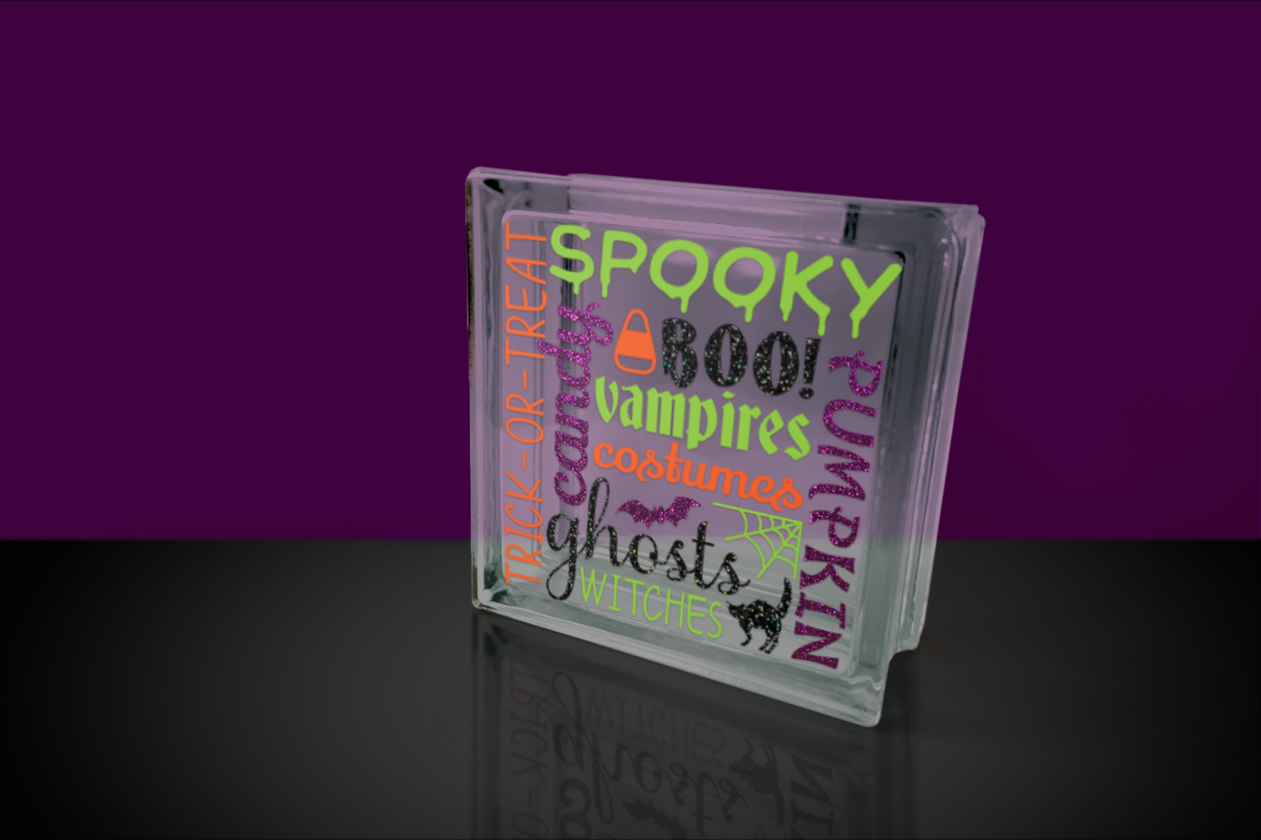 Glass block with subway word art design. Features words related to Halloween. Also includes a bat, a cat, a candy corn, and a spiderweb nestled within the words.