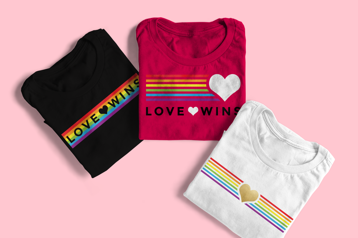 Three folded tees. The left tee has rainbow stripes with the phrase "love wins" knocked out with a heart in the middle. The middle tee has a large heart with rainbow stripes to the left of it and the phrase "love wins" below with a heart in the center of the words. The right tee has a heart in the middle with rainbow stripes to the left and right.