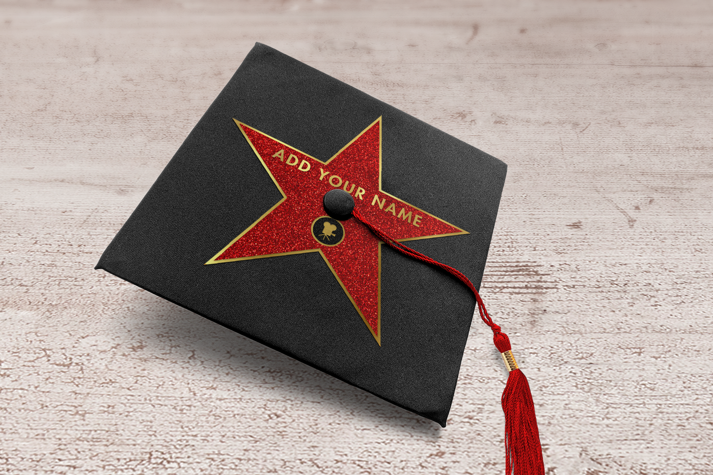 Grad cap with a red star and gold outline. It says "add your name" in gold letters and there is an icon of a movie camera in a circle.