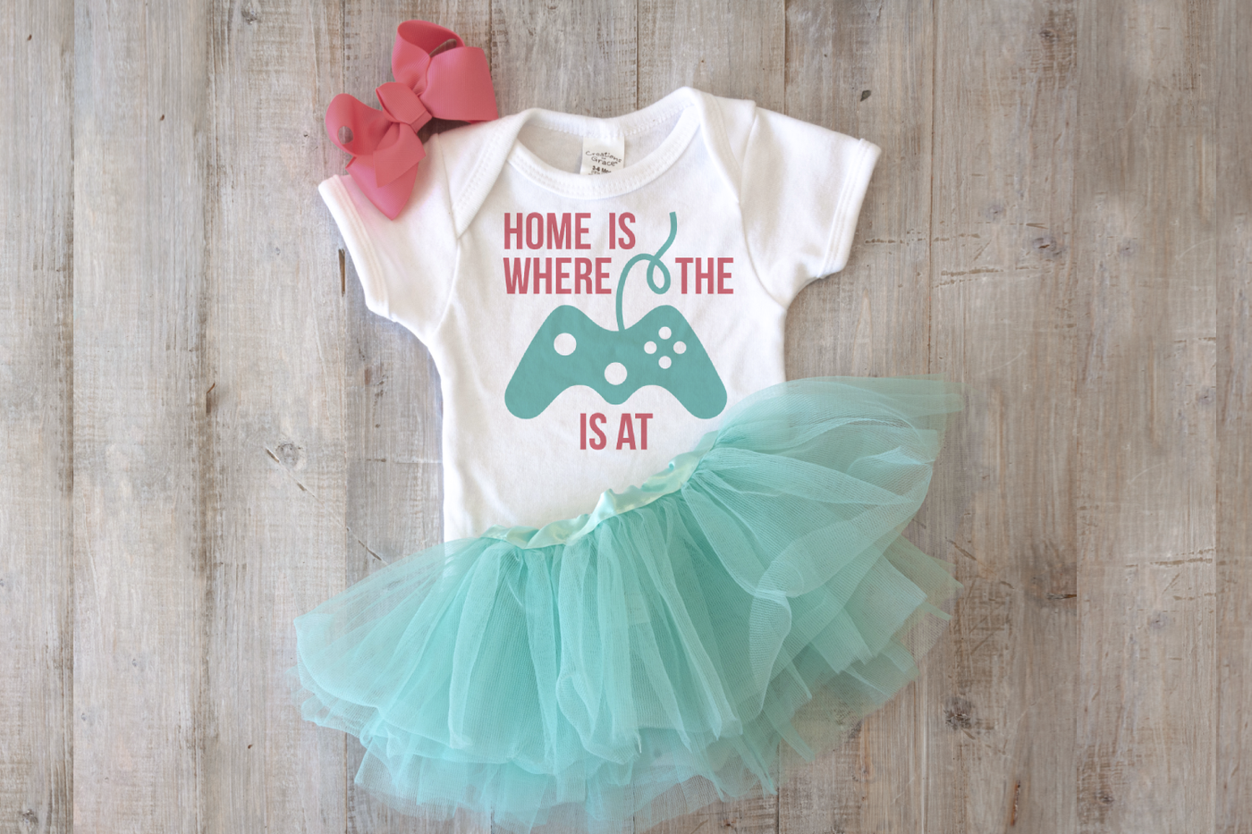 Baby onesie with a design that has a video game controller and text that reads "home is where the [game controller] is at."