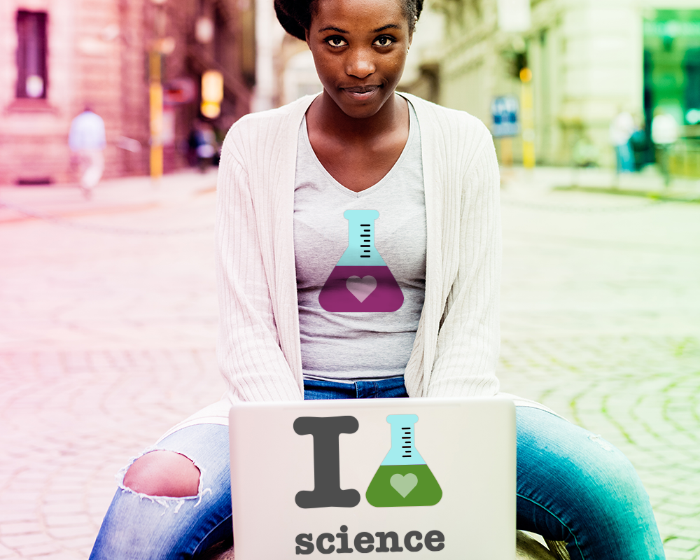 A black woman sits with an open laptop. On the lap top is a design that says "I heart science." the heart is on a filled beaker. On her shirt is also a filled beaker with a heart in the liquid.