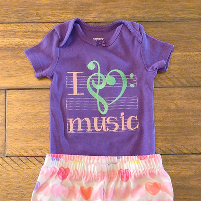 Embroidery design that says "I heart music." the words are against a sheet music staff. The heart is formed by a bass and treble clef symbol that looks like a heart.