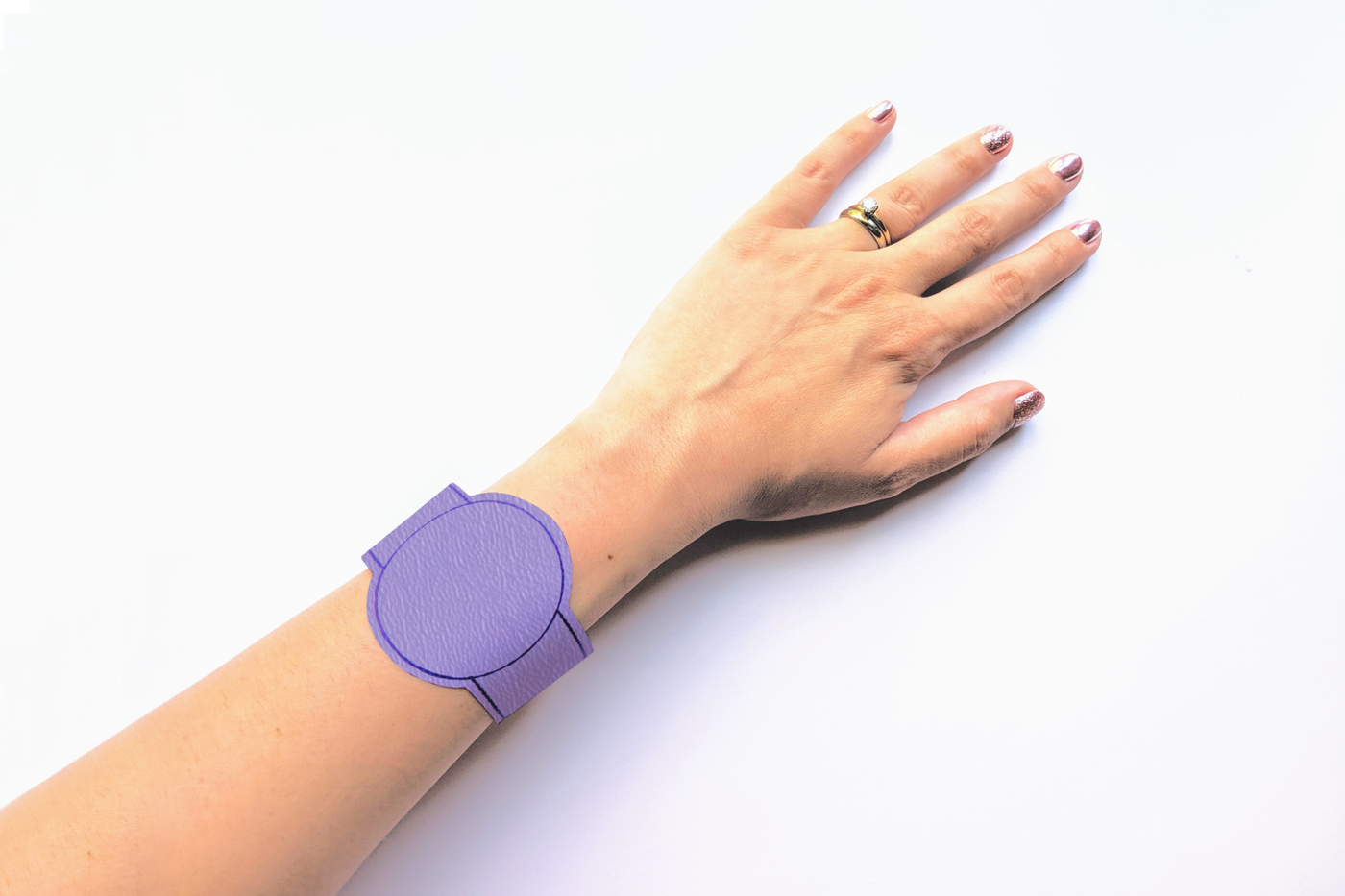 The lower arm of a white presenting-Latinx woman. She wears a purple faux leather bracelet with a circle in the middle.