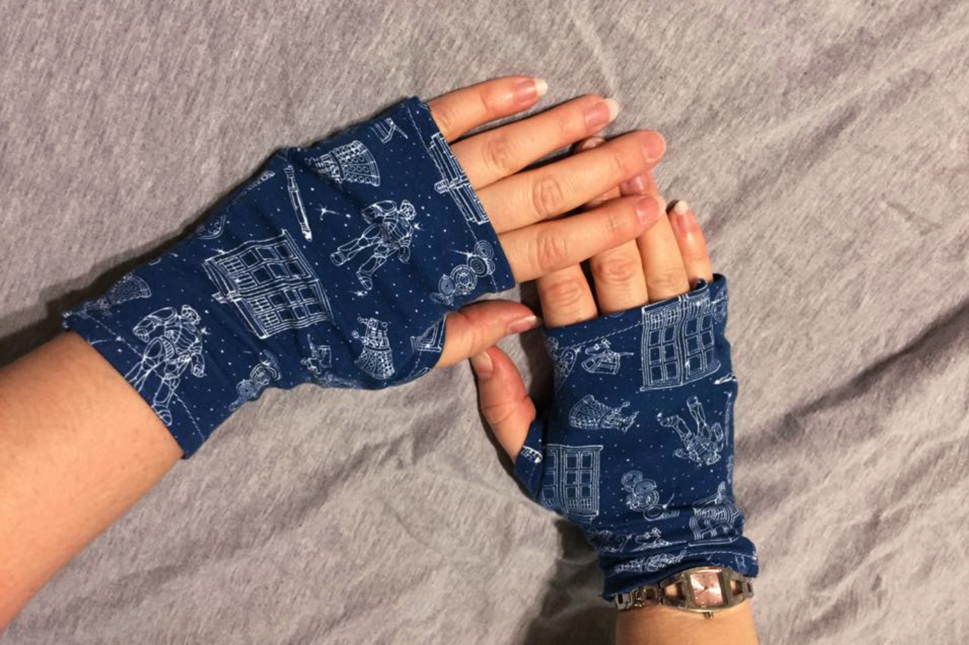 A pair of white women's hands wearing fingerless gloves in a blue and white Doctor Who fabric.