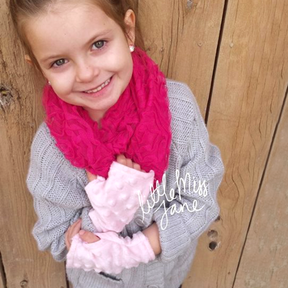 White little girl wearing a pair of pink fleece fingerless gloves.