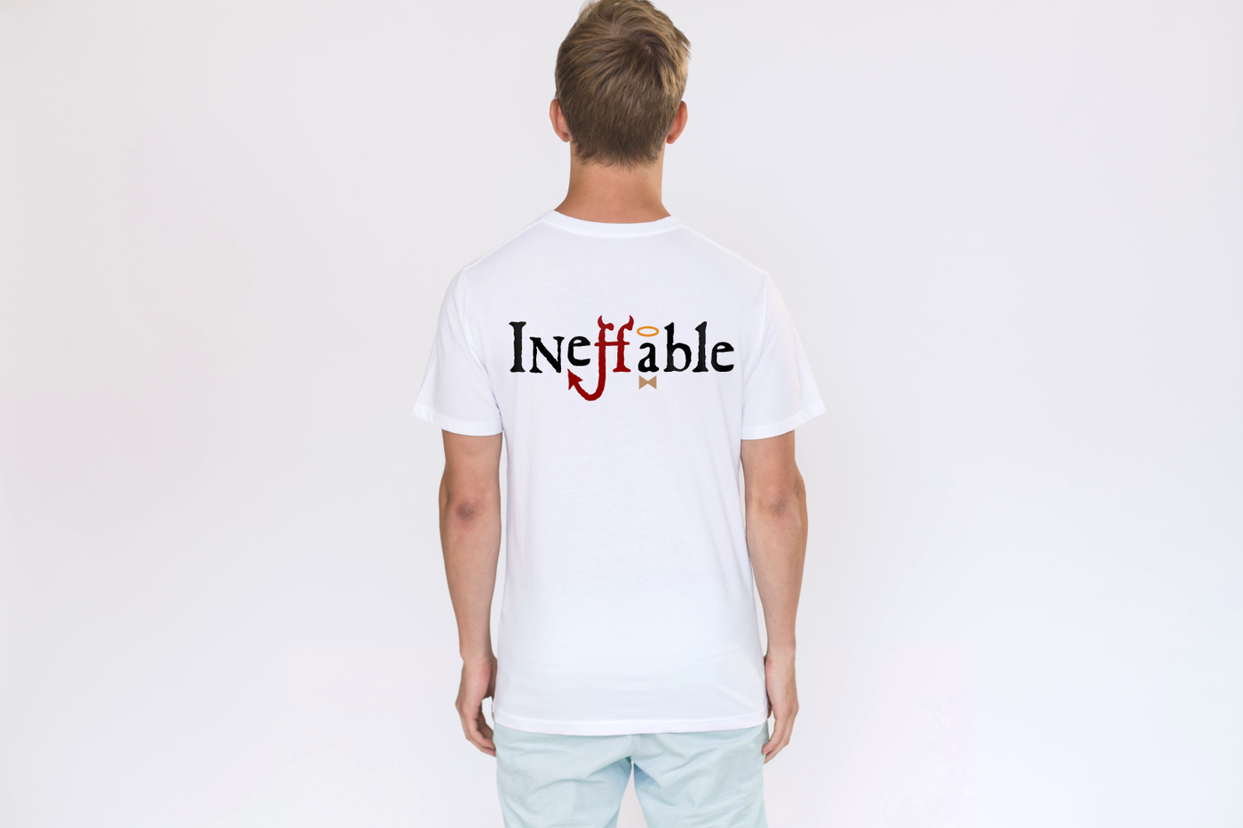 White man facing a white wall, visible from the back. His white tee has the word "Ineffable" on it. The fs have devil horns and a tail, and the a has a halo and bow tie.