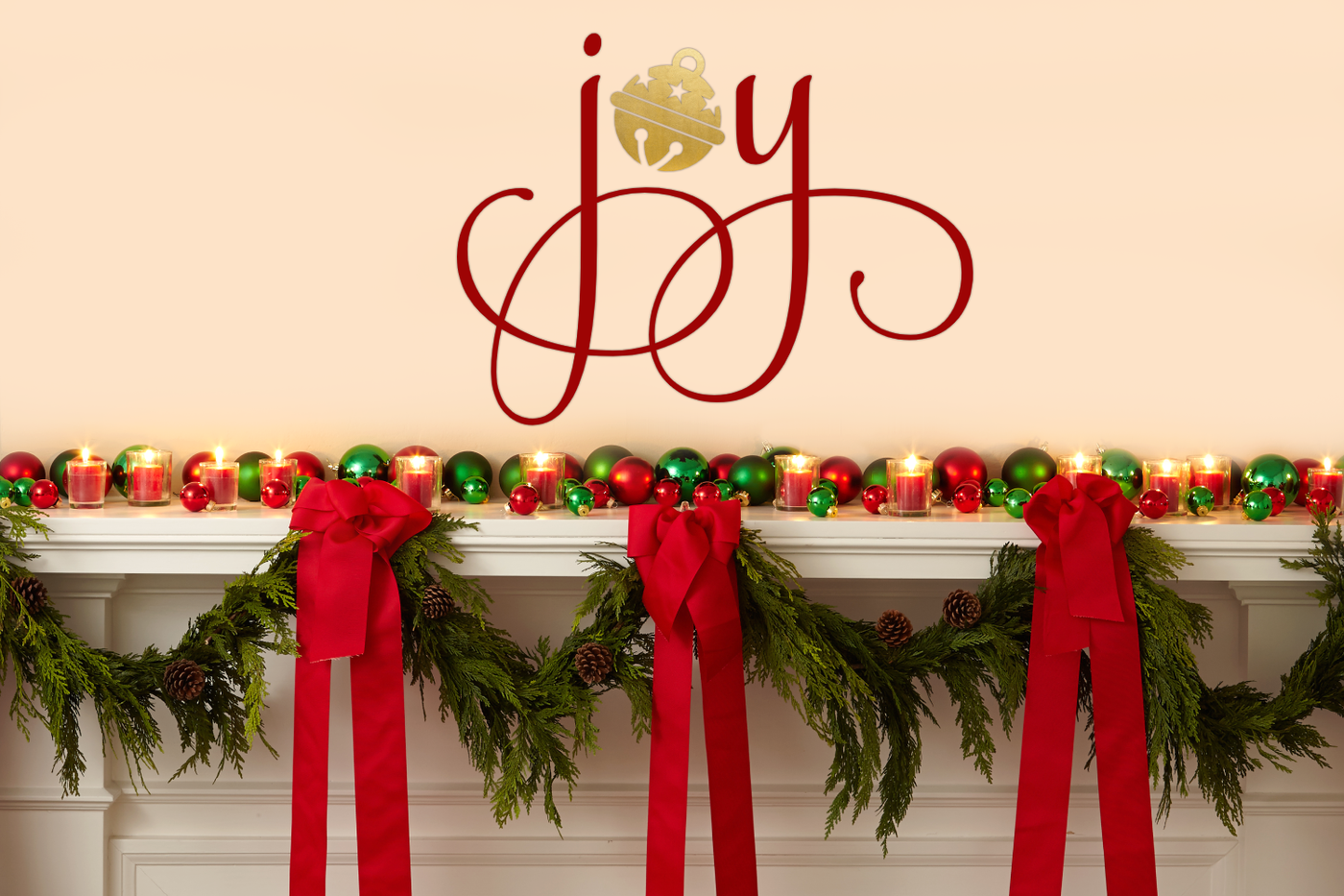 A mantle decorated for Christmas. Above the mantle on the wall is the word "joy" in elegant script. In place of the O is a round bell.