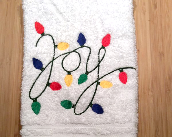 Towel embroidered with the word "Joy" written out of a string of holiday lights.