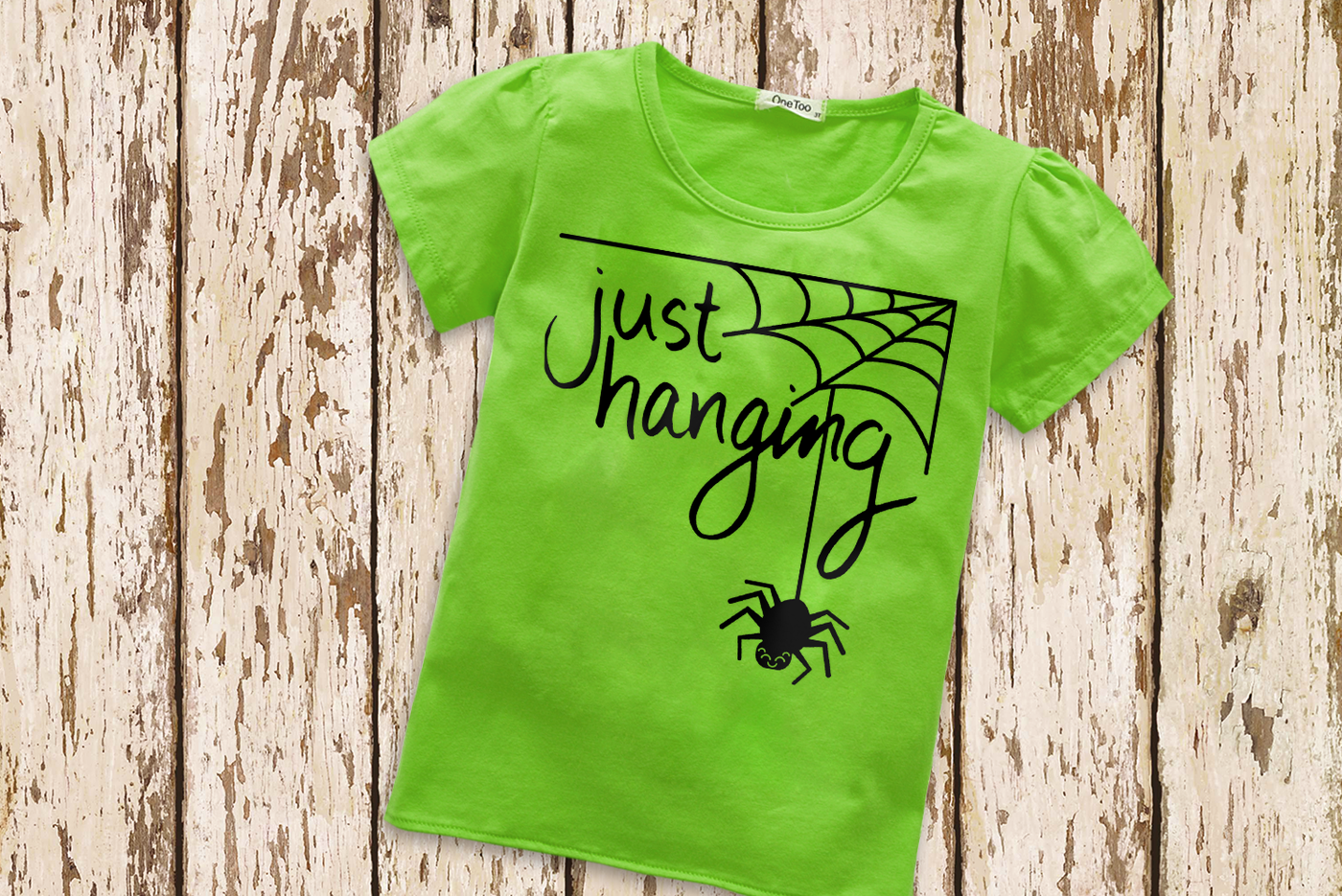 Green tee with a spiderweb with a cute smiling spider and the text "just hanging."