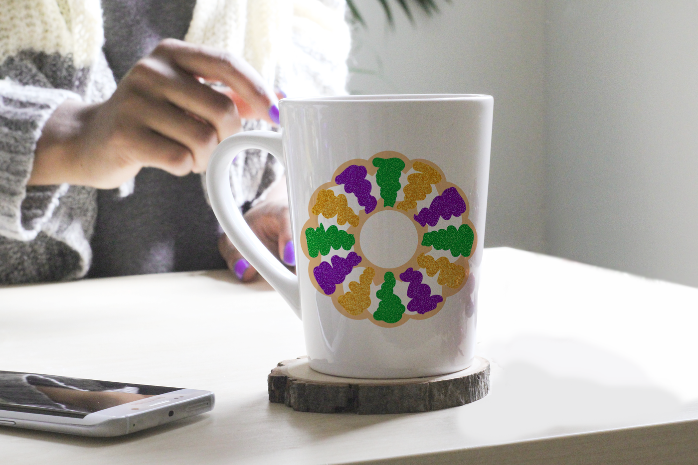 Black woman reaching for a mug with a King Cake design.