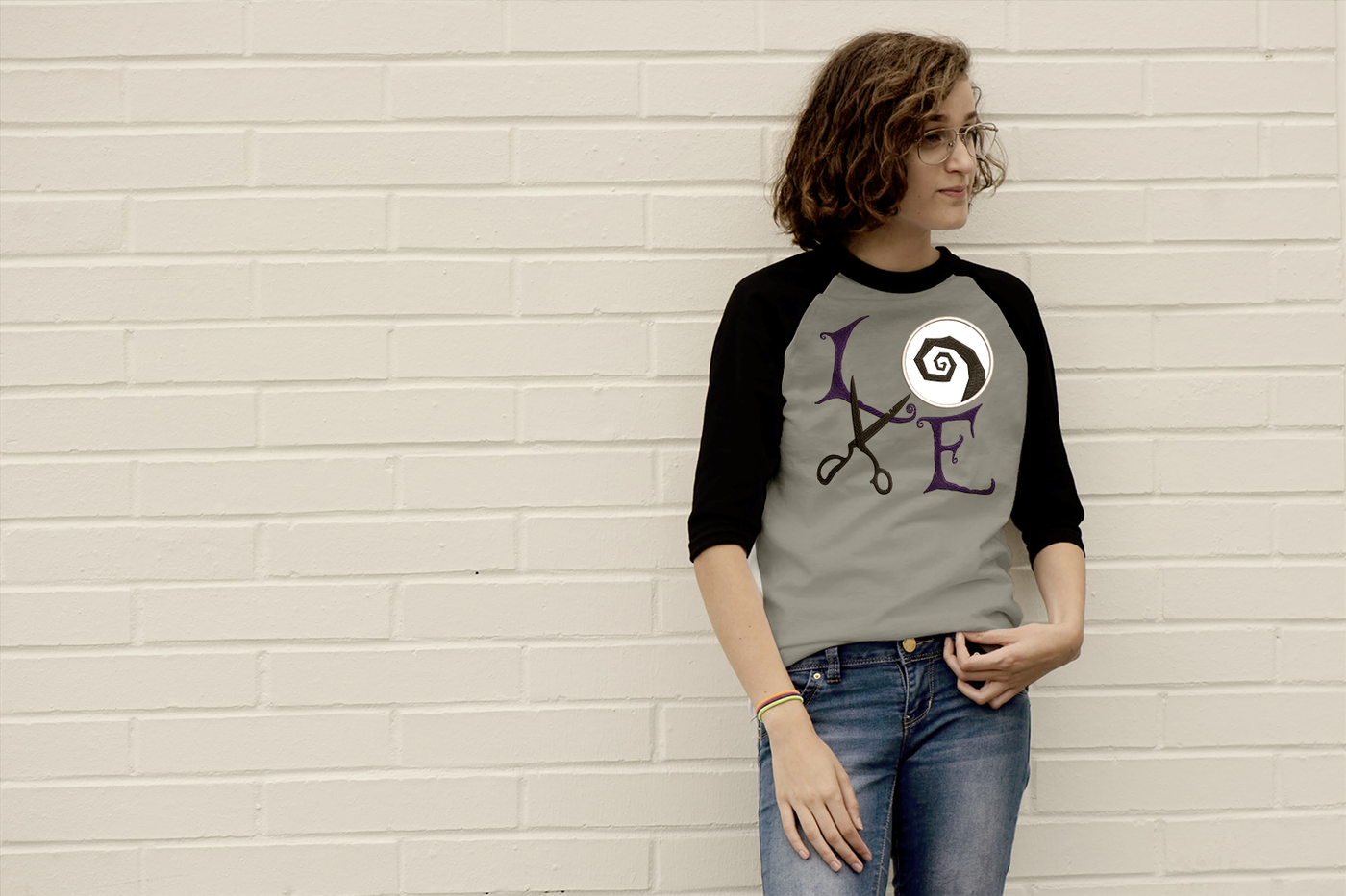 White-presenting teen girl wears a raglan tee with the applique word "LOVE" set on a square. The letters are in gothic style. In place of the O is a circle with a rough swirl embroidery. In place of the V are a pair of old scissors.