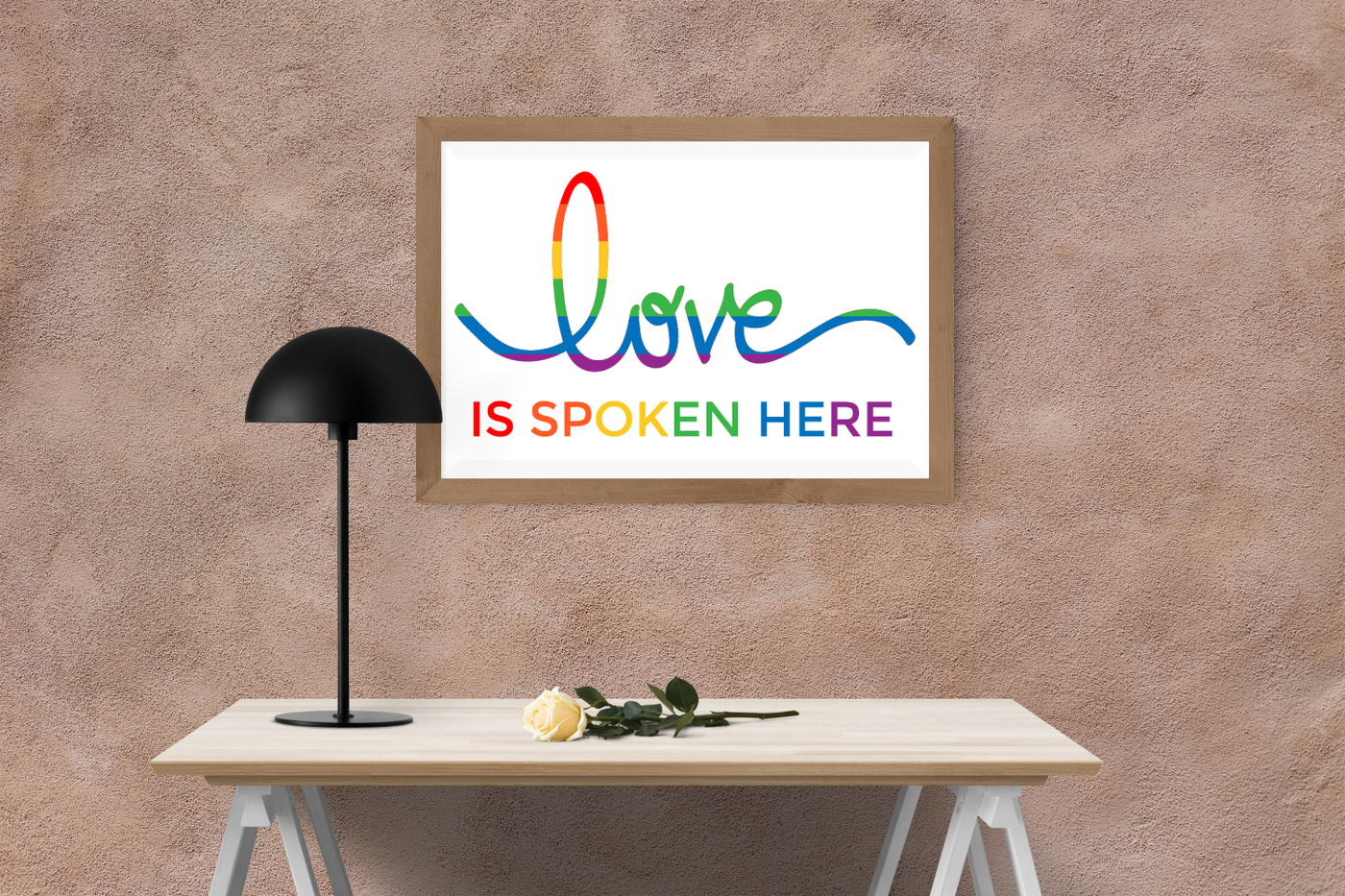 Framed poster above a desk says "love is spoken here" in rainbow letters.
