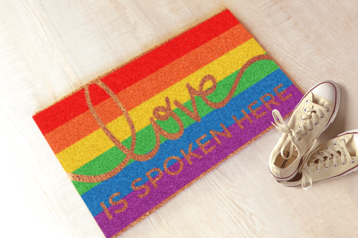 Doormat with rainbow stripes. Knocked out of the stripes is the phrase "love is spoken here."