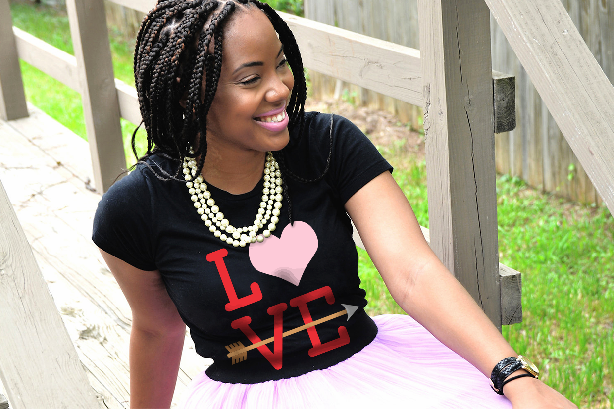 A smiling black woman wears a shirt that says "LOVE" with a heart and arrow on the design