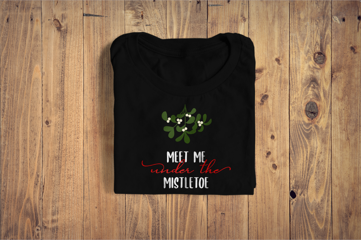 A shirt with a design that says "meet me under the mistletoe" with a sprig of mistletoe.