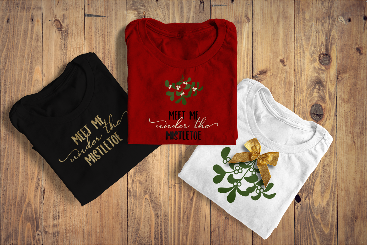 Three shirts. Two say "meet me under the mistletoe." One has a sprig of mistletoe over the text. The third shirt has only the mistletoe and has a real bow on top.