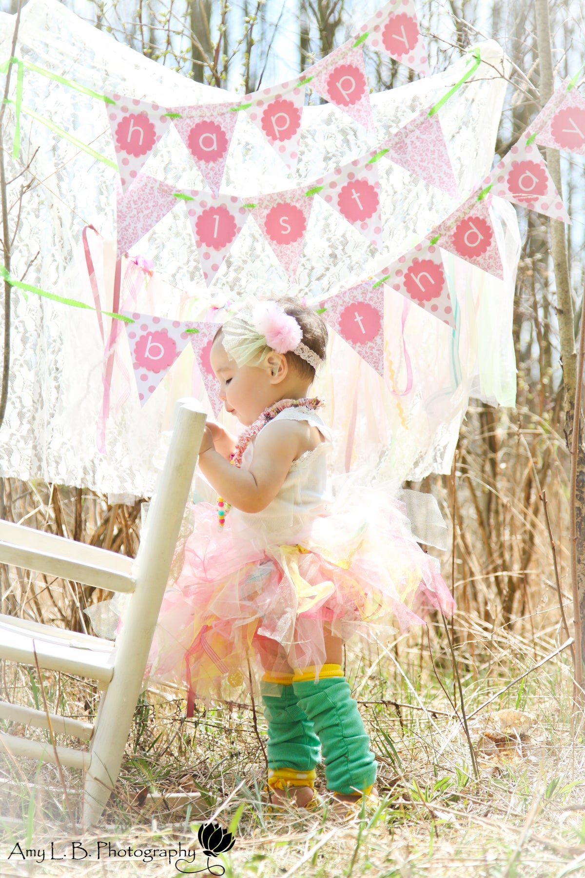 Asian baby girl in a tutu standing in front of a flag banner that says "happy 1st birthday."