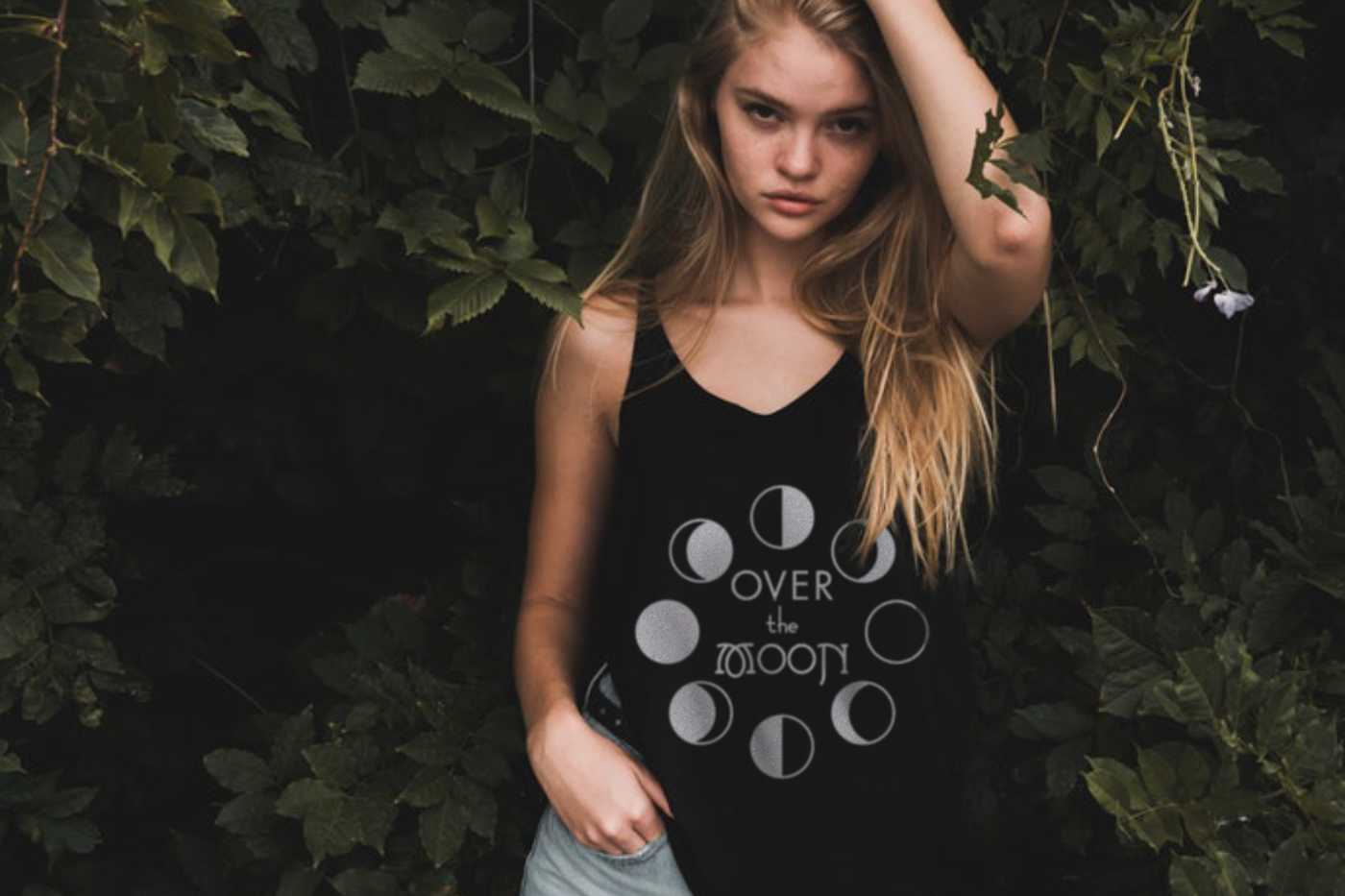 White woman in a tank top that has the phases of the moon with the text "Over the moon."