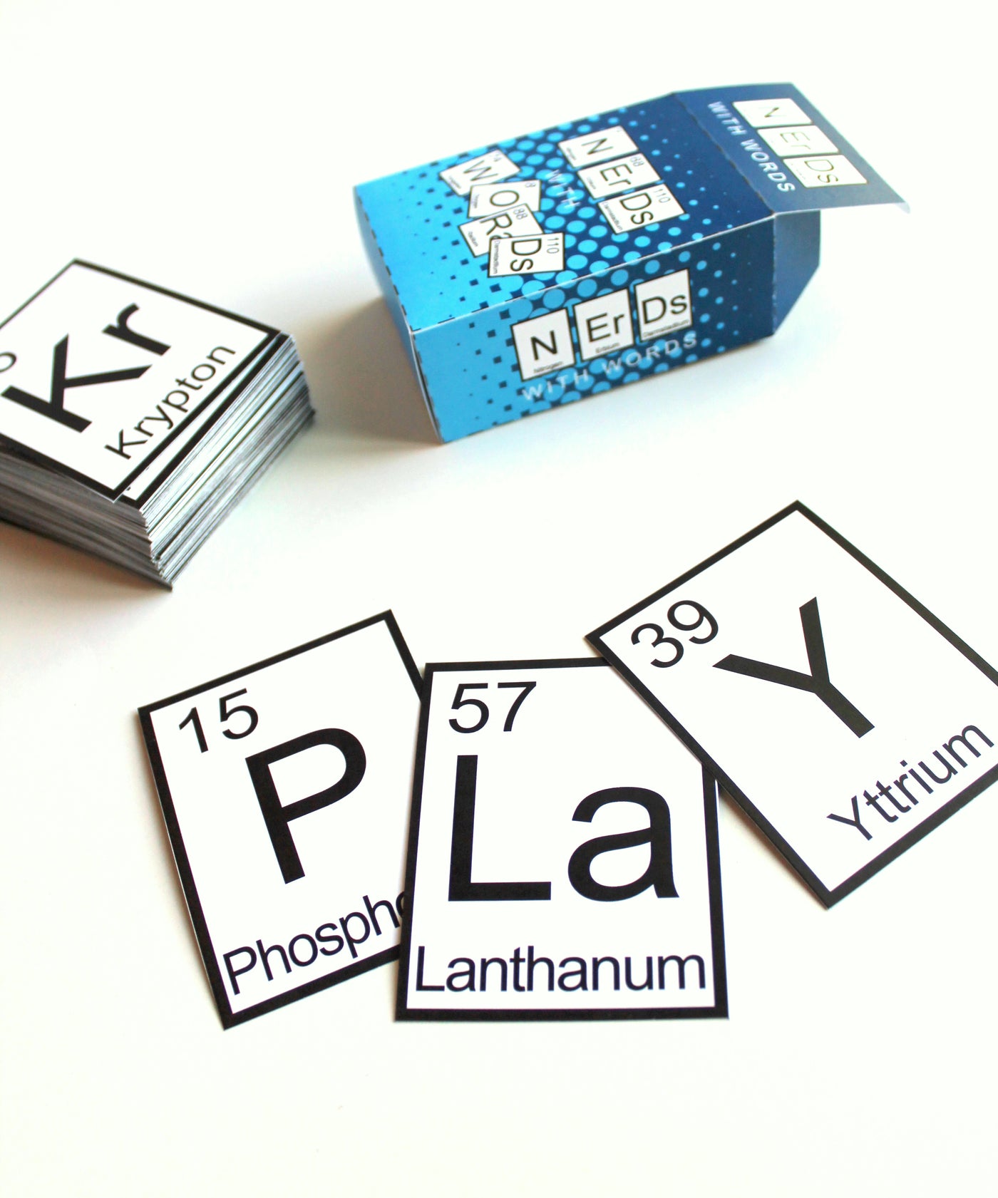 A stack of cards. Each has a different periodic element. Three cards are fanned out to spell "PLaY." The card box is blue and says "Nerds with Words."