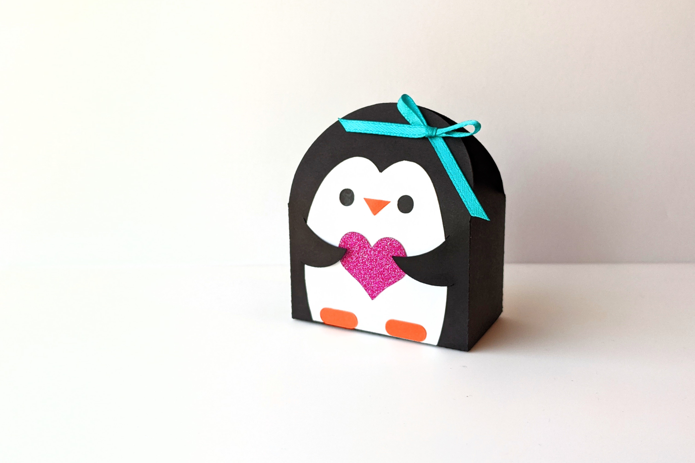 Penguin shaped gift box SVG design. The penguin holds a heart.