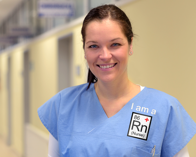 White woman wearing scrubs that say "I am a RN (Nurse)." The RN looks like a periodic element.