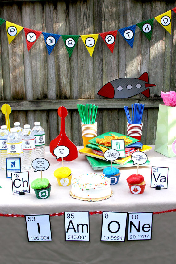 A decorated party table with a banner in front that says "I Am ONe" made out of period table elements.