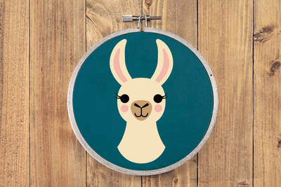 An embroidery hoop with teal fabric. In the center is the image of a smiling llama from the neck up.