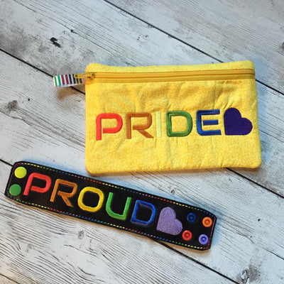 Black faux leather bracelet embroidered with "PROUD" with a heart in rainbow colors. ellow zippered bag with the embroidered word "PRIDE" and a heart in rainbow colors.