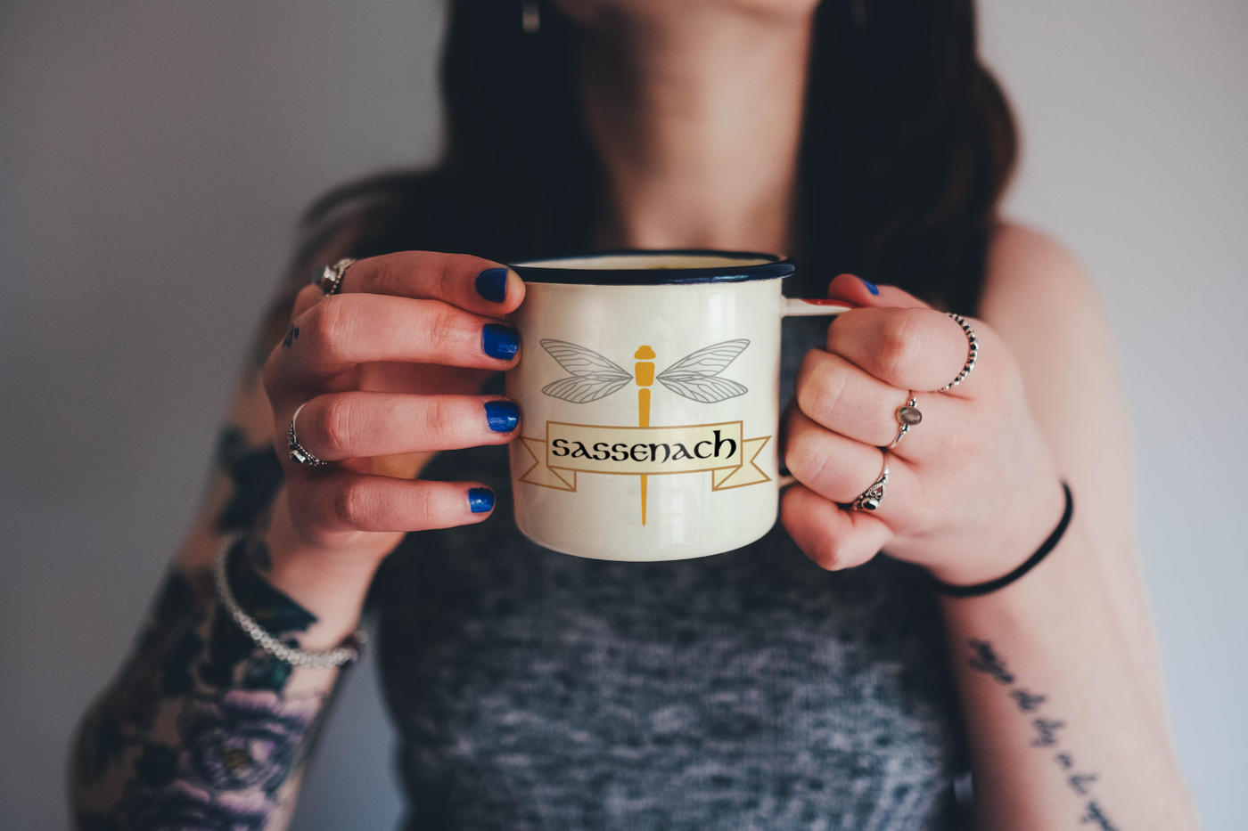 White woman holds a mug that has a dragonfly design with a banner that says "Sassenach"