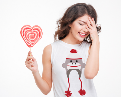 White woman laughing and holding a lollipop. Her shirt has a sock monkey hat design.