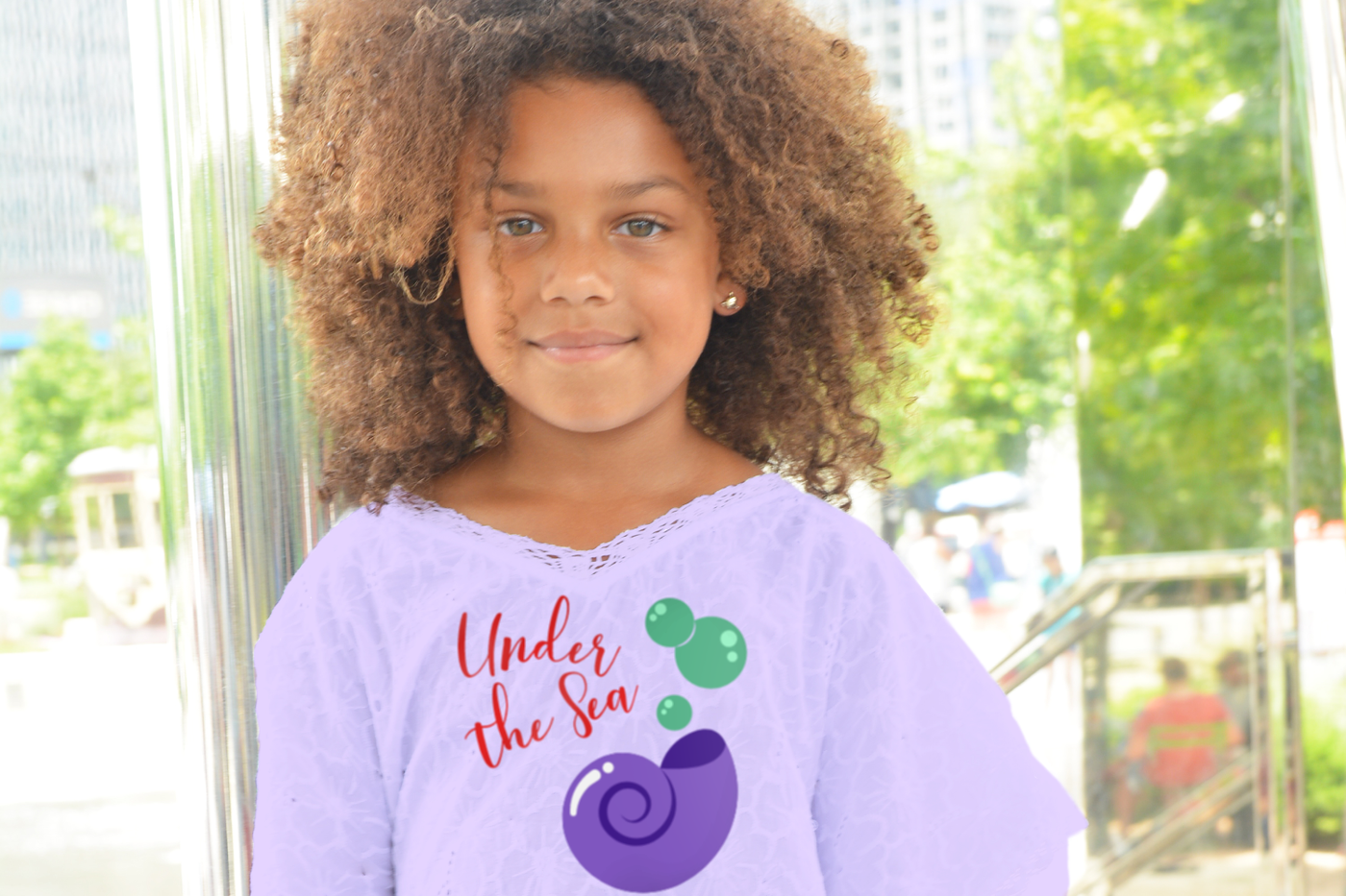 Black little girl wearing a lavender shirt with a seashell design that says "under the sea"