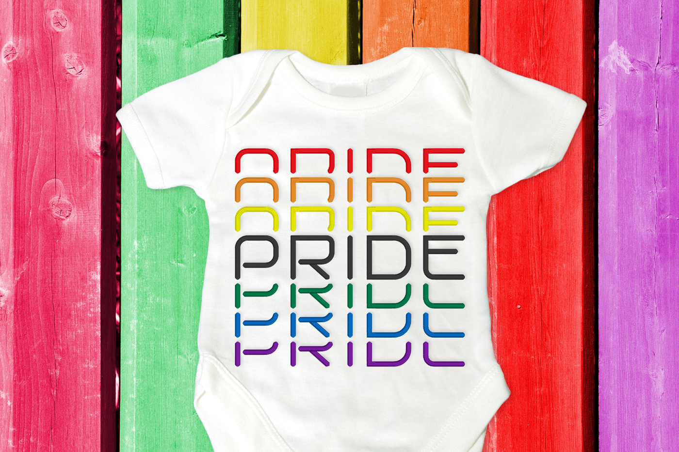Stacked Pride embroidery design shown stitched on a white onesie on a rainbow painted wood background.