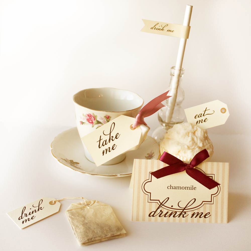 A tea bag with a "drink me" tag, a tea cup with a "take me" tag, a cupcake with an "eat me" tag, a straw with a "drink me" flag, and a table tent labeled "chamomile drink me." The tags are all in ivory with brown print.