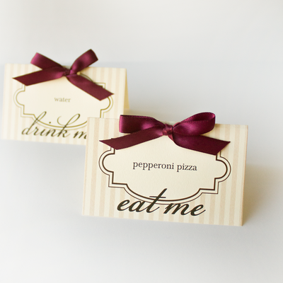 Two table tents on ivory paper with tan stripes and burgundy bows. The tents say "water" and "pepperoni pizza." Underneath they say "drink me" and "eat me."