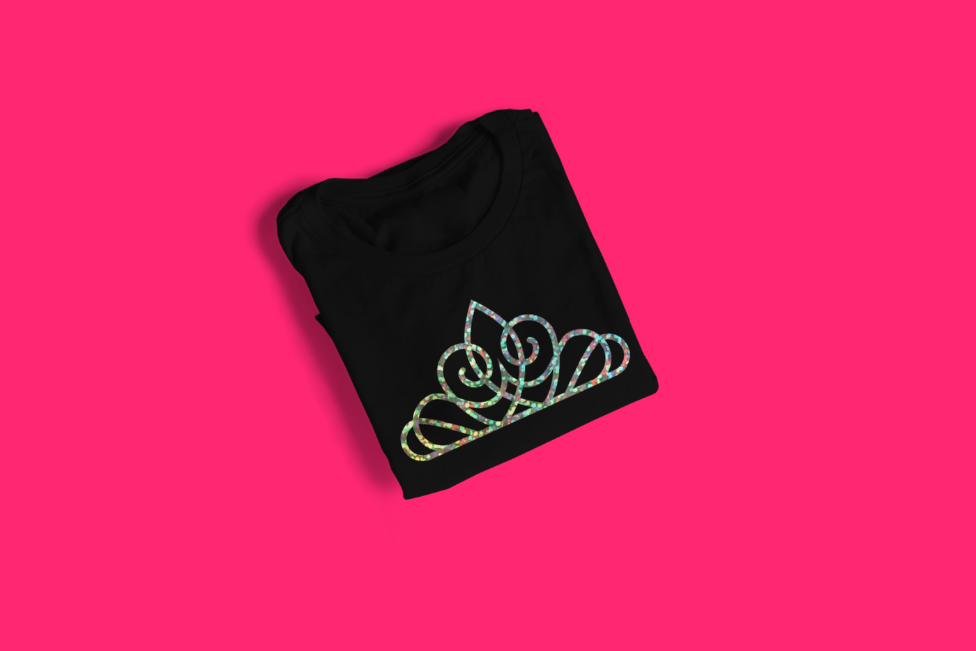 A black folded tee on a hot pink background. In the center is a tiara done in holographic heat transfer vinyl.