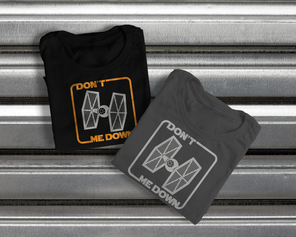 Two folded tees. Each has a Tie fighter with a rounded square around it that has the words "Don't" and "Me Down." When red with the Tie Fighter, it makes the parody phrase "Don't tie me down."
