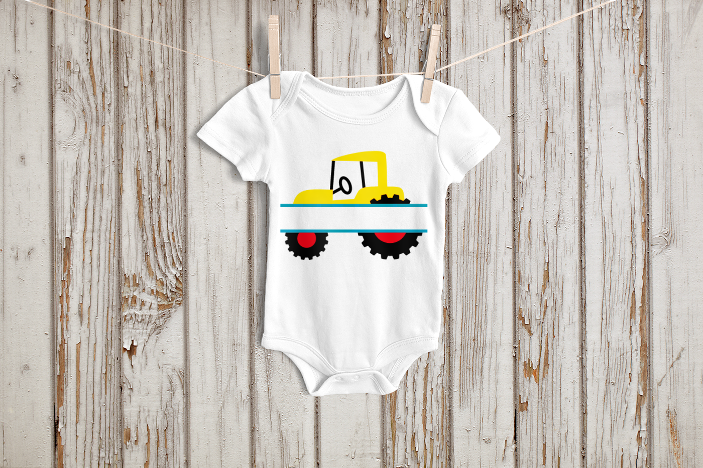 A white baby onesie hanging on a clothesline. On it is a tractor design split in the middle.