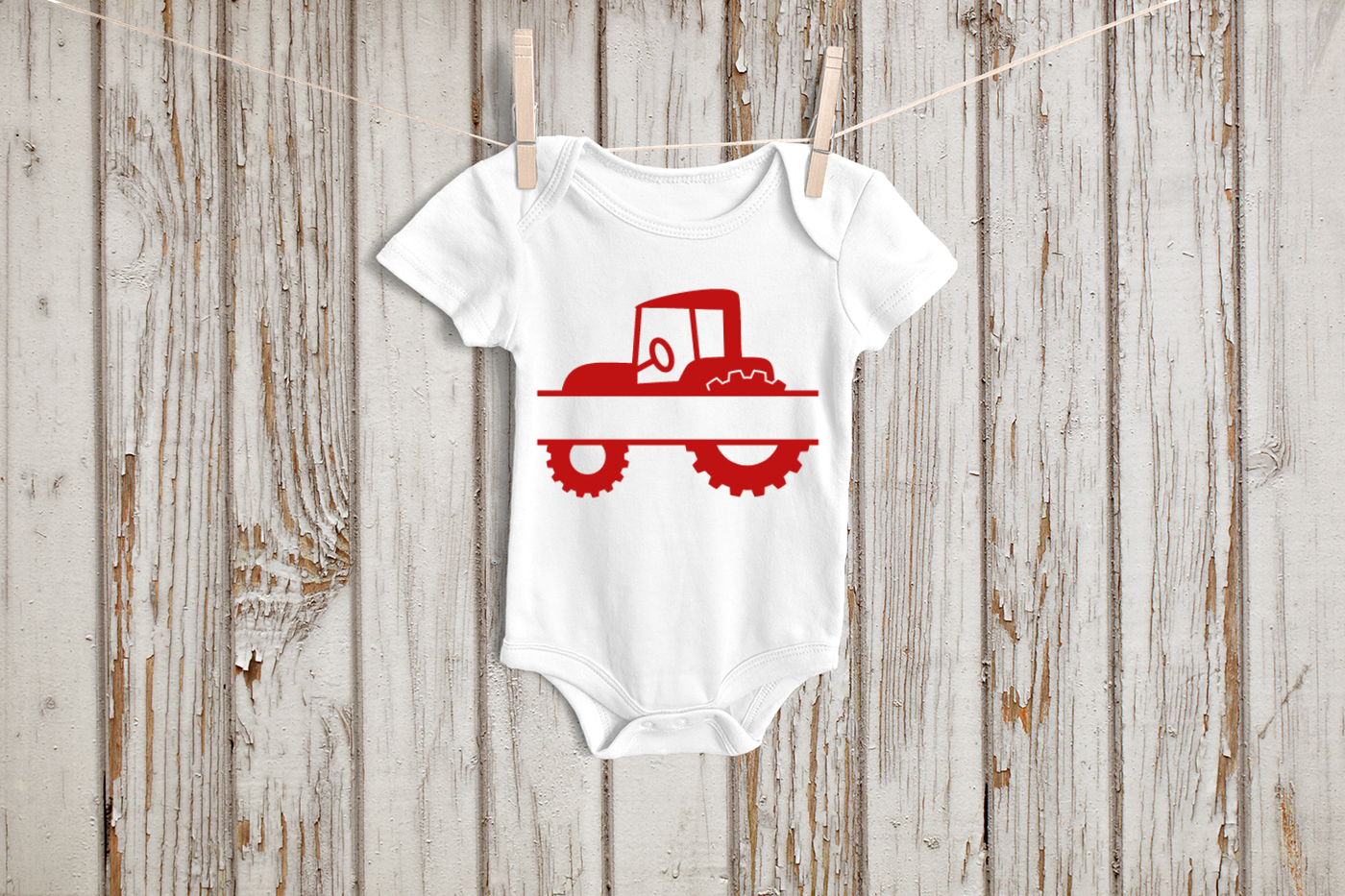 A white baby onesie hanging on a clothesline. On it is a tractor design split in the middle.