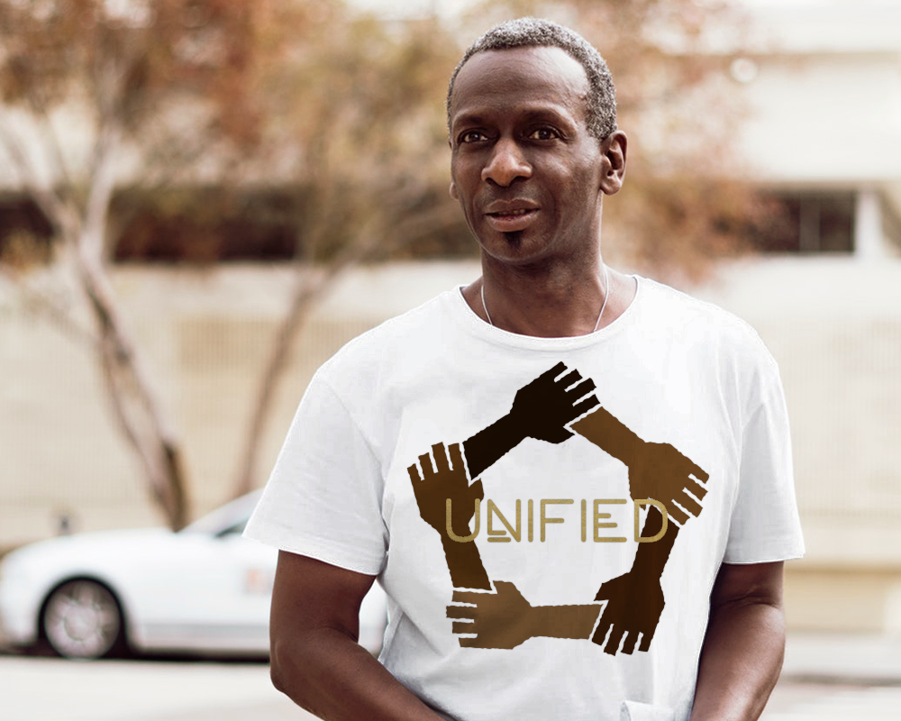 A black man stands outside with a car and tree in the background, out of focus. He wears a white tee with 5 linked hands in different shades of brown. In the center is the word "Unified" in gold.