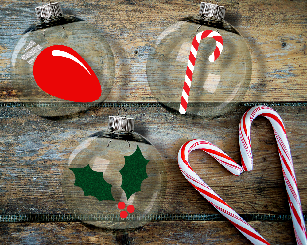 Three clear round Christmas ornaments. One has a Christmas light bulb, one a candy cane, and one a sprig of holly.