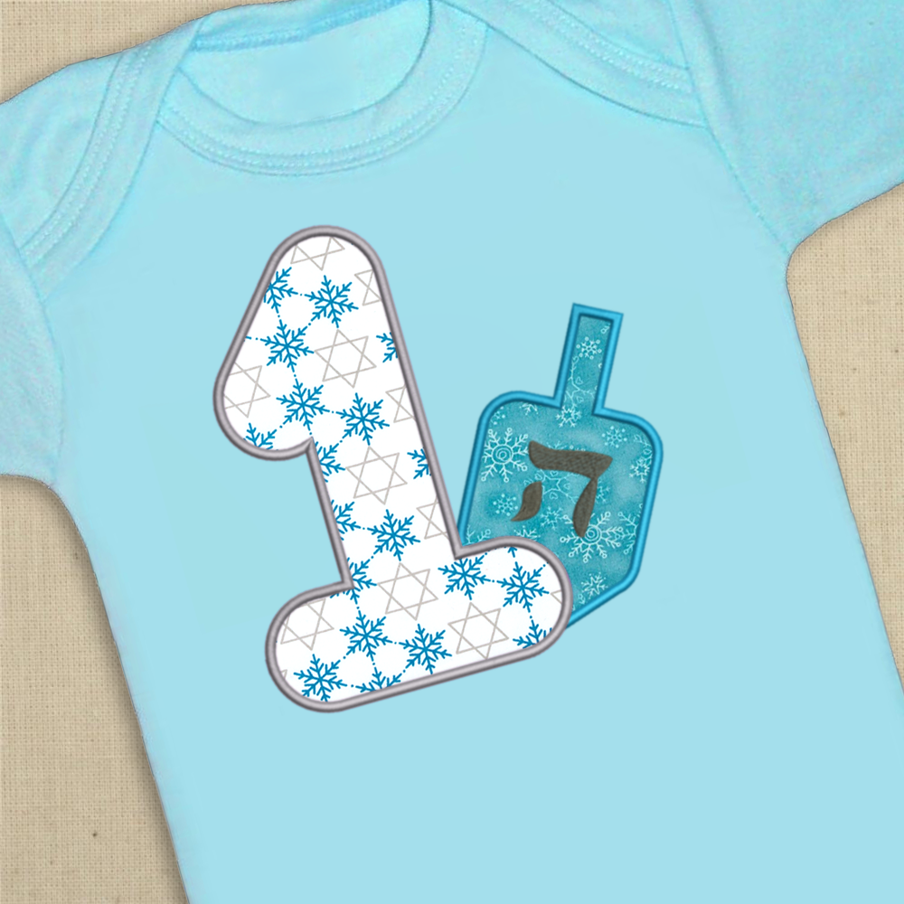 Blue onesie with a large applique 1. Behind the number is an applique dreidel.